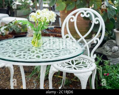 Weiß schmiedeeisernen Tisch mit weißen Blume in Vase auf Glasplatte und Stuhl Vintage-Stil im Garten. Stockfoto