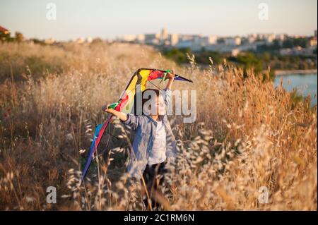 Glücklich entzückend lächelndes kleines Kind mit Drachen in den Händen stehen auf Sommerfeld nea Seehafen außerhalb der Stadt Stockfoto