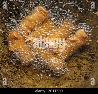Nahaufnahme von frittierten Frühlingsrollen, die in heißem Öl in einem großen Wok in der Küche gebraten werden. Die Frühlingsrollen blasen und drehen sich goldbraun im heißen Öl Stockfoto