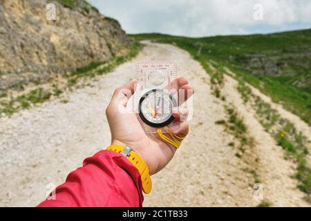 Männliche Hand hält einen magnetischen Kompass auf dem Hintergrund von Hügeln und den Himmel mit Wolken. Das Konzept des Reisens und Findens Stockfoto