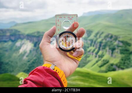 Männliche Hand hält einen magnetischen Kompass auf dem Hintergrund von Hügeln und den Himmel mit Wolken. Das Konzept des Reisens und Findens Stockfoto