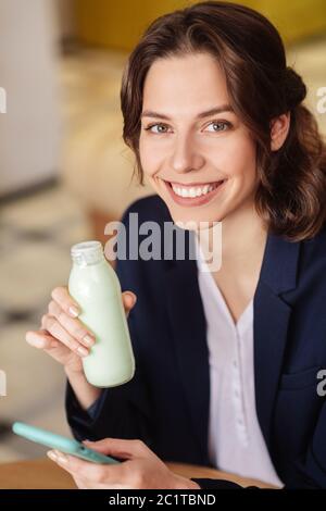 Schönes Mädchen mit braunen Augen halten Joghurt und Smartphone Stockfoto
