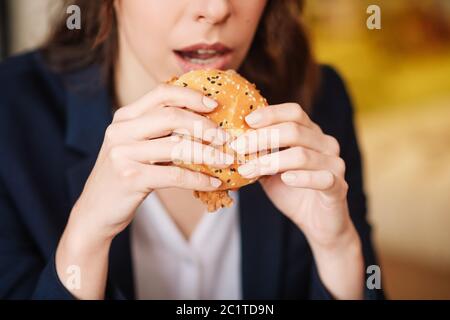 Weibliche Hände halten einen Burger in der Nähe des Mundes. Stockfoto
