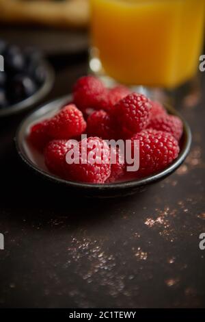 Nahaufnahme auf frische Himbeeren auf Keramik Untertasse auf dunklen rusty Tabelle gelegt. Stockfoto