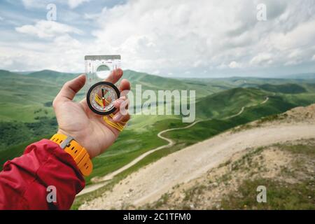 Männliche Hand hält einen magnetischen Kompass auf dem Hintergrund von Hügeln und den Himmel mit Wolken. Das Konzept des Reisens und Findens Stockfoto