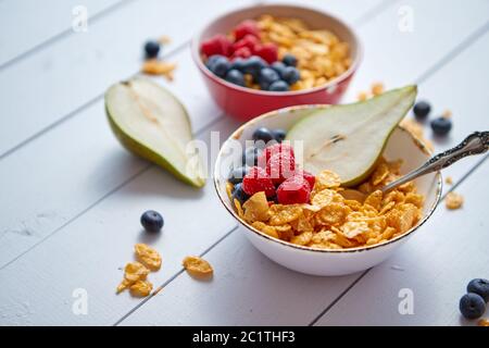 Golden Cornflakes mit frischen Früchte Himbeeren, Heidelbeeren und Birne in Keramik Schüssel Stockfoto