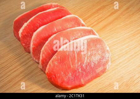 Fünf Stücke Schweinefleisch auf einem Brett mit einer Holzstruktur gehackt Stockfoto