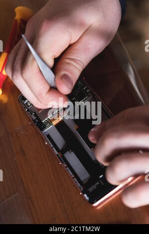 Nahaufnahme der Hand eines Heimwerkers, der ein zerlegtes Smartphone repariert. Das Konzept der Selbstreparatur-Elektronik zu Hause Stockfoto