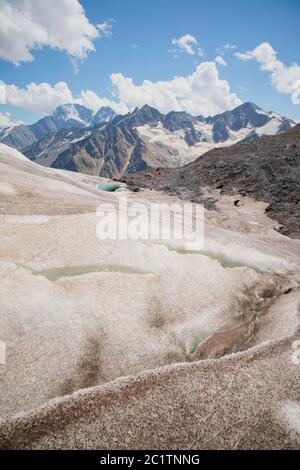Berglandschaft staubige schmutzige vulkanische Abhang mit einem rissigen schmelzenden Gletscher vor der Kulisse der Kaukasus-Berge. Glo Stockfoto
