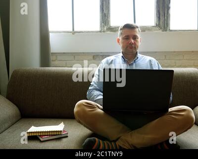 Mann mit Laptop arbeitet zu Hause. Quarantänekonzept. Freelancer sitzt auf dem Sofa und gibt auf der Tastatur ein. Stockfoto