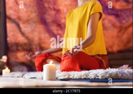 Nahaufnahme der Hand einer Frau in einer Yoga-Lotuspose, die in einem Handwerkerraum mit Kerzen meditiert Stockfoto