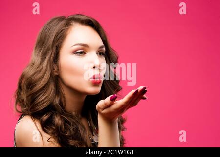 Portrait einer Schönheit, die Kuss an die Kamera sendet. Das Mädchen hat lange schöne dunkle Haare, rosa Studio Hintergrund Stockfoto