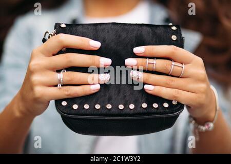 Mädchen mit gepflegten Nägel mit schönen Ornament in Trauringe Holding schwarzes Fell Tasche. Stockfoto