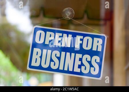 Nahaufnahme eines blauen geöffneten Schildes im Schaufenster eines Geschäfts mit der Meldung „für Unternehmen geöffnet“. Stockfoto
