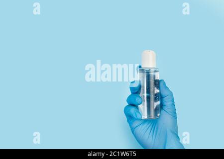 Hand mit einem blauen medizinischen Handschuh, der eine Flasche Gelalkohol auf hellblauem Hintergrund hält Stockfoto