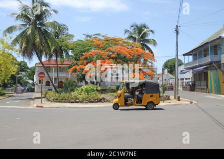 Kleiner Park mit Flammenbaum und Tuk-Tuk-Taxi in Andoany/Hell-Ville City Centre Square, Madagaskar. Stockfoto