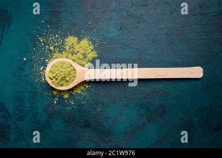 Holzlöffel gefüllt mit grünem Matcha-Teepulver mit etwas Pulver, das auf smaragdgrünen Hintergrund ausgegossen wurde. Japanischer Matcha Tee ist Luxus Bio-bever Stockfoto