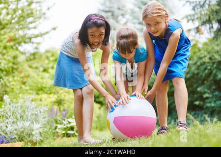 Drei glückliche Kinder spielen zusammen mit einem Ball im Garten Stockfoto