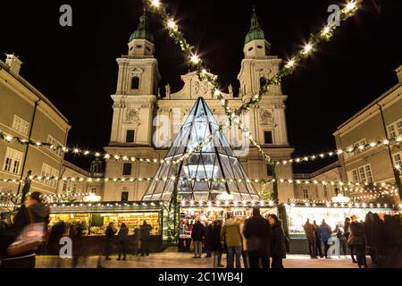 SALBURG, ÖSTERREICH - 11. DEZEMBER 2015: Dekorationen und Gebäude auf dem Salzburger Christkindlmarkt im Domplatz bei Nacht. Menschen können gesehen werden. Stockfoto