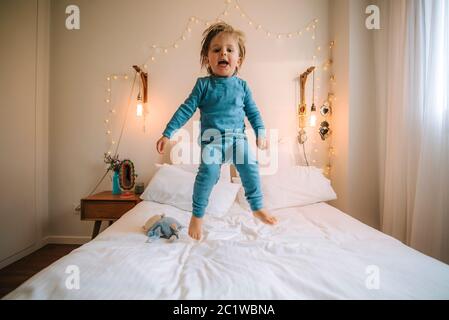 Kleiner blonder Junge hat Spaß beim Springen und Spielen auf einem großen Bett. Familie zu Hause. Coronavirus. Quarantäne. Stockfoto