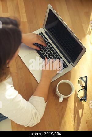 Draufsicht auf die Hände der Frauen, die auf dem Laptop-Tastenfeld mit Brille und Kaffee tippen Stockfoto