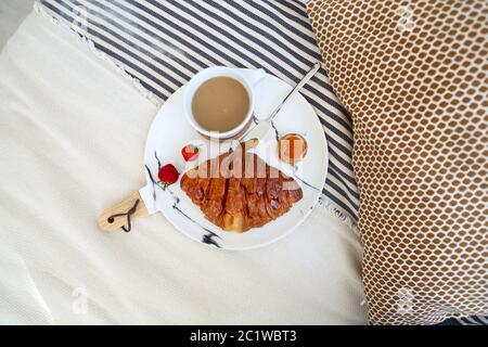 Frühstück mit Croissant, Kaffee, Erdbeere und Marmelade auf dem Teller Tablett im Bett Stockfoto