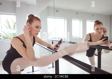Kaukasische Balletttänzerin, die ihr Bein streckt und ihr Smartphone benutzt