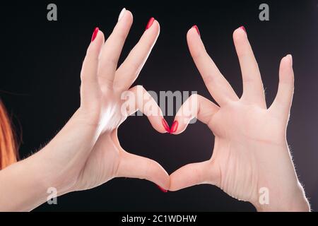 Isoliert liebe Werbetechnik durch die Hände mit roten gepflegte Nägel Studio auf schwarzem Hintergrund. Stockfoto