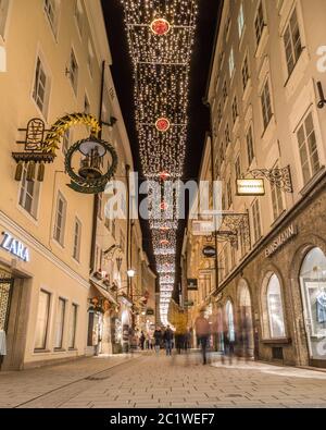 SALBURG, ÖSTERREICH - 20. DEZEMBER 2017: Blick in die Getreidegasse in Salzburg bei Nacht während der Weihnachtszeit. Dekorationen, Menschen, Geschäfte und Bui Stockfoto