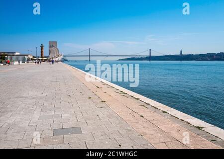 Blick nach Osten zum Monument der Entdeckungen und zur Brücke vom 25. April, auf der Promenade des Flusses Tejo in Belém, Lissabon, Portugal. Stockfoto