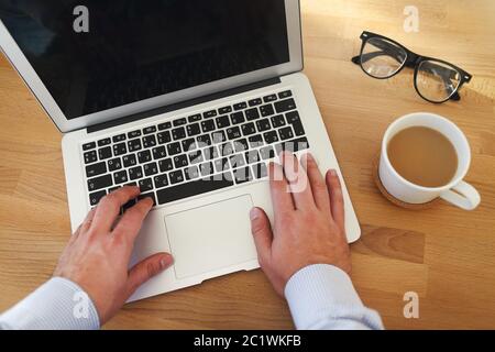 Draufsicht auf den Mann, der am Laptop arbeitet und eine Tasse Kaffee trinkt Stockfoto
