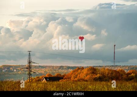 Bunte große heiße Luft Herz geformten Ballon fliegen gegen den bewölkten Himmel auf dem Land an einem Herbstabend Stockfoto