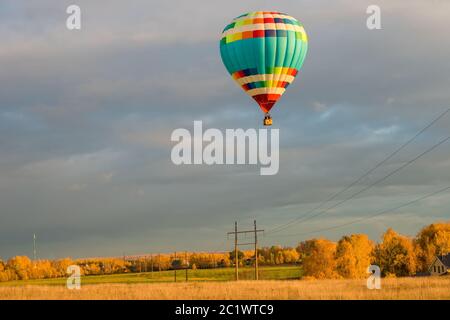 Bunte große Heißluftballon fliegen gegen den bewölkten Himmel in der Landschaft an einem Herbstabend Stockfoto