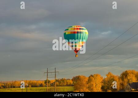 Bunte große Heißluftballon fliegen gegen den bewölkten Himmel in der Landschaft an einem Herbstabend Stockfoto