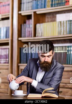 Reifer Mann mit ruhigem Gesicht hat eine Tasse Tee. Der Geschäftsmann sitzt im Vintage-Interieur und genießt entspanntes Lesen. Bärtiger Mann in Luxusanzug in der öffentlichen Bibliothek. Entspannen, Vergnügen, Freizeit, Hobby-Konzept. Stockfoto