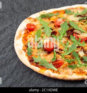 Saftige Pizza auf dem Tisch mit Kirschtomaten und Ruccola Stockfoto