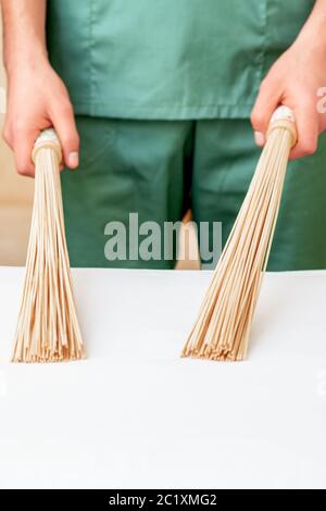 Nahaufnahme der Hände des Masseurs, der Bambus-Massagebsen auf dem Tisch hält. Stockfoto