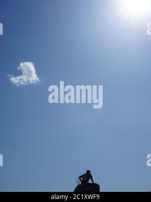 Ein Mann ruht auf einem Felsen, an einem sonnigen Sommertag. Der Himmel ist blau und hat eine herzförmige Wolke. Stockfoto