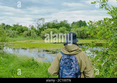 Aktiver Mann in Moskitoanzug mit Rucksack beim Wandern in der Nähe Waldsee in sibirien, russland. Alleinreisen, Lifestyle, inländisches Tourismuskonzept Stockfoto