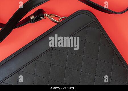 Schwarze Handtasche mit Zierrhombussen auf rotem Hintergrund, Draufsicht, flach liegend. Kein Logo, kein Name. Einkaufskonzept. Stockfoto