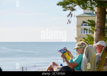 Ein älteres Paar entspannt sich auf Liegestühlen über Cottesloe Beach in Perth Western Australia mit dem Strand und dem riesigen Indischen Ozean vor ihnen Stockfoto