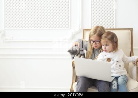 Liebenswert kleine Schwestern mit ihrem Computer Laptop zusammen mit ihrem Kätzchen Stockfoto