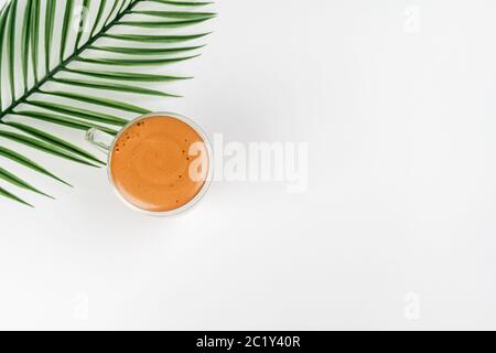 Kaffee in einer Glasschale auf weißem Hintergrund mit Blättern. Platz für Text kopieren. Cappuccino mit köstlichem Karamellschaum Stockfoto