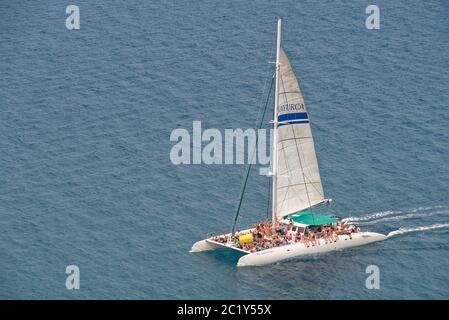 Katamaran voller junger Leute auf einer Party-Bootstour entlang der Küste der Llevant Halbinsel, nahe Port d’Alcudia, Mallorca Nordostküste, August. Stockfoto