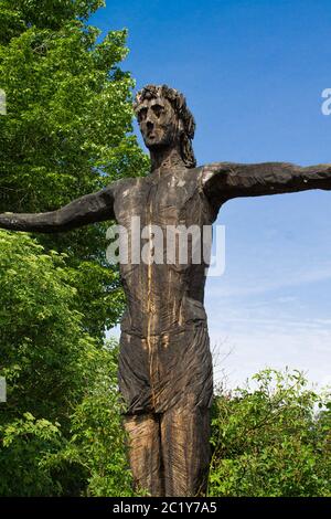 Seitenansicht Bild einer hölzernen Statue von Jesus, der in voller Pose mit ausgebreiteten Armen mit einem blauen Himmel im Hintergrund steht Stockfoto