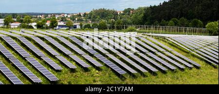 Kleiner Photovoltaik-Solarpark mit schwarzen Paneelen auf einem kleinen Hügel mit einem Dorf im Hintergrund Stockfoto