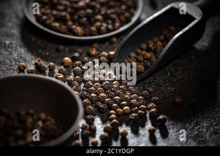 Schwarze Pfefferkörner in schwarzer Holzschaufel Stockfoto