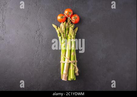 Konzept eines Strauß Spargel und Kirschtomaten in Form einer Blume auf dunklem Hintergrund. Draufsicht mit Kopierbereich Stockfoto