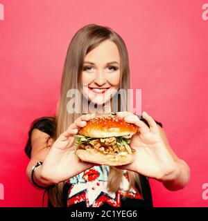 Ziemlich lächelnde Mädchen mit Hamburger in die Hände im Vordergrund. Stockfoto