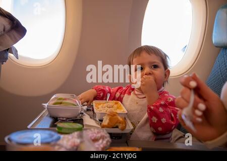 Niedliche Kleinkind Flugzeug Passagier isst spezielle Baby an Bord Mahlzeit Umfliegen Flug Stockfoto